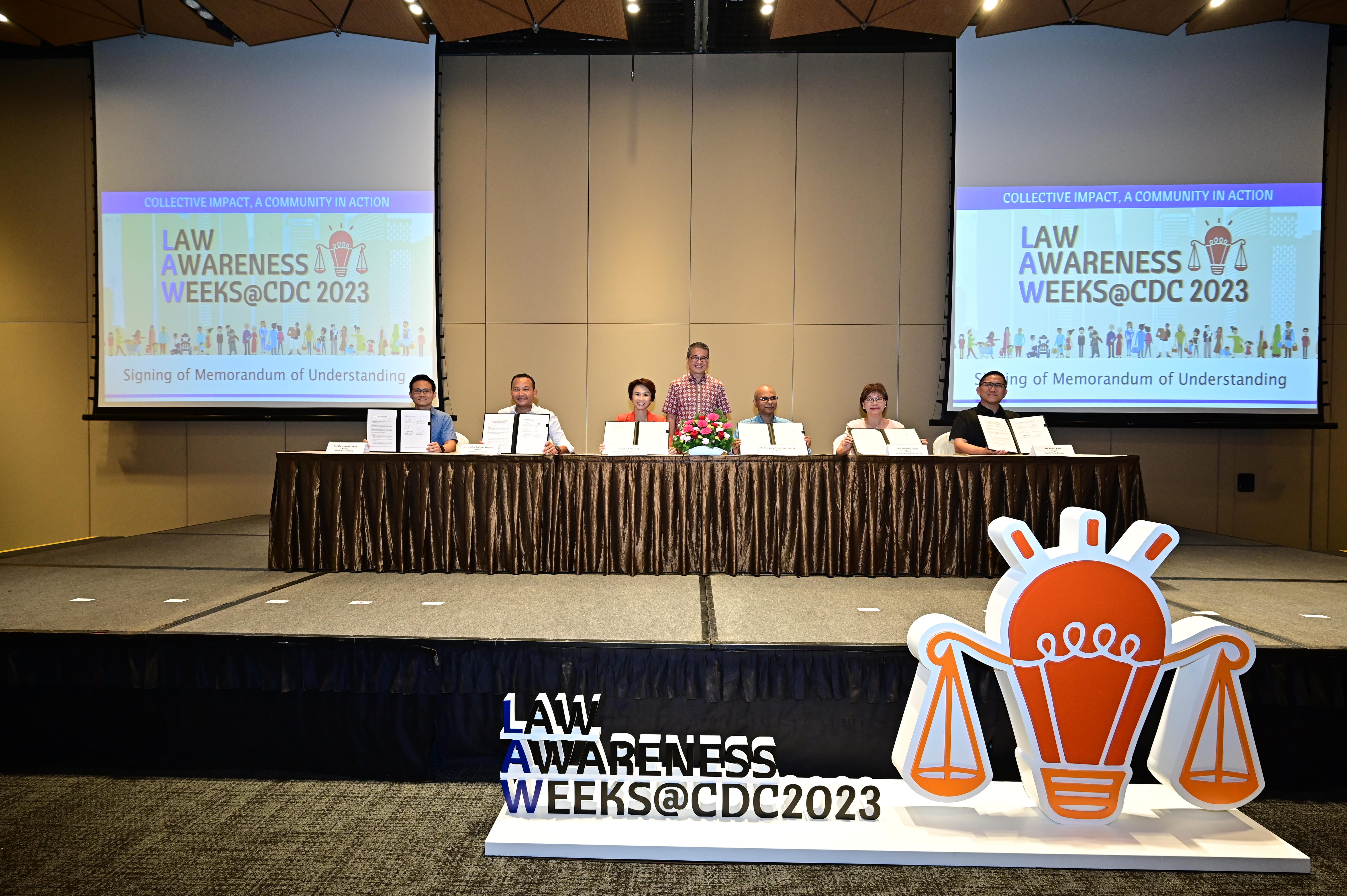 Six people display documents while seated at a table, with large screens showing "Law Awareness Weeks@CDC 2023."